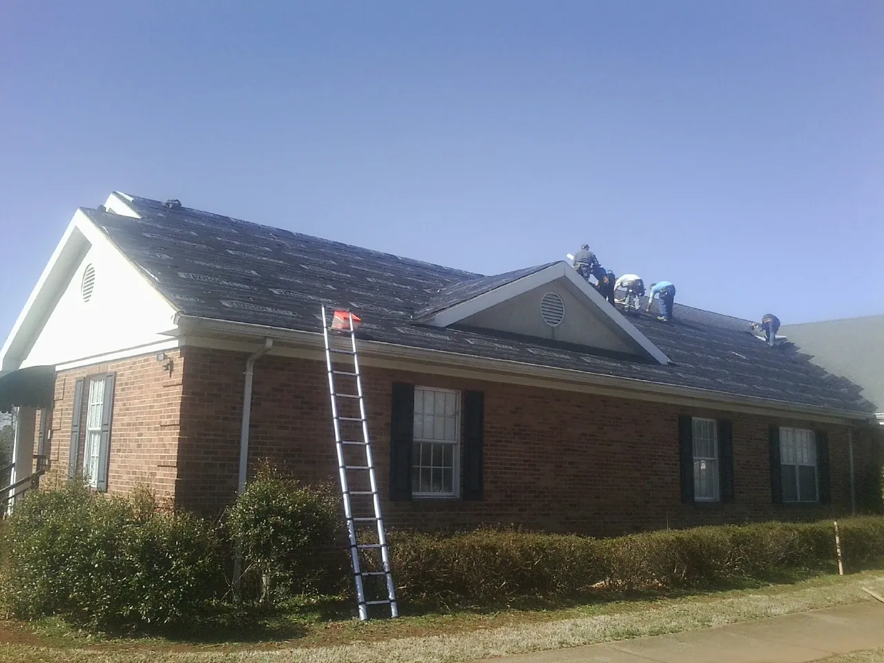 Crew tearing shingles off a brick ranch roof with a ladder set — Emergency Roof Repair work by our crew in Paw Paw