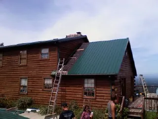 Green metal roof going on a two story log home with ladders set in Paw Paw