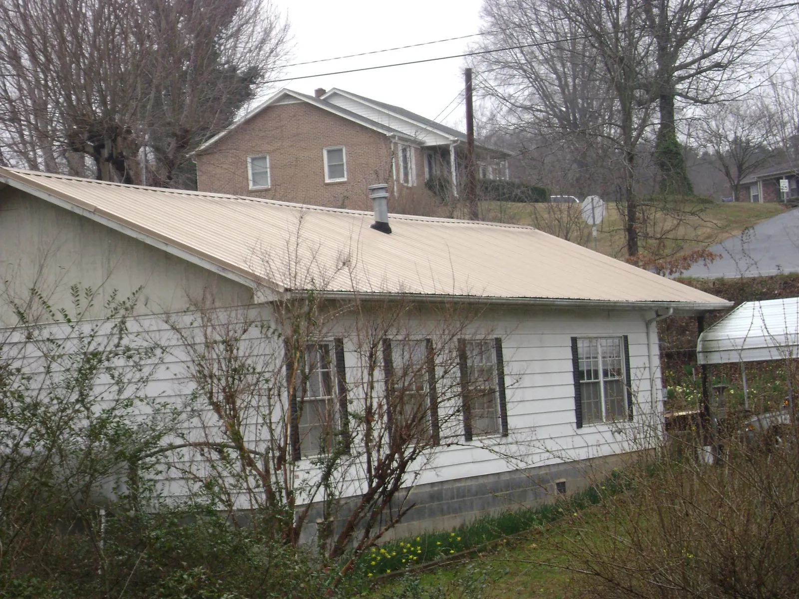 Tan metal roof on a white sided house set into a hillside — Commercial Roofing by Roofing Brothers in Paw Paw