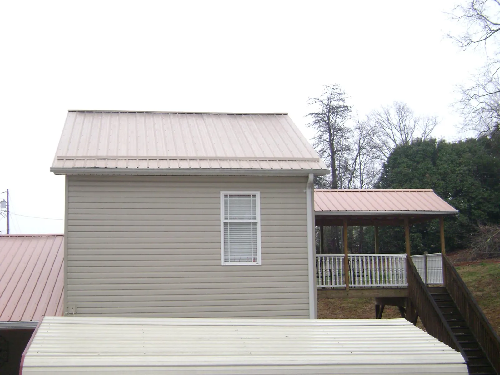 Tan metal roofs on a two story addition and attached porch, from a Roof Replacement job in Paw Paw